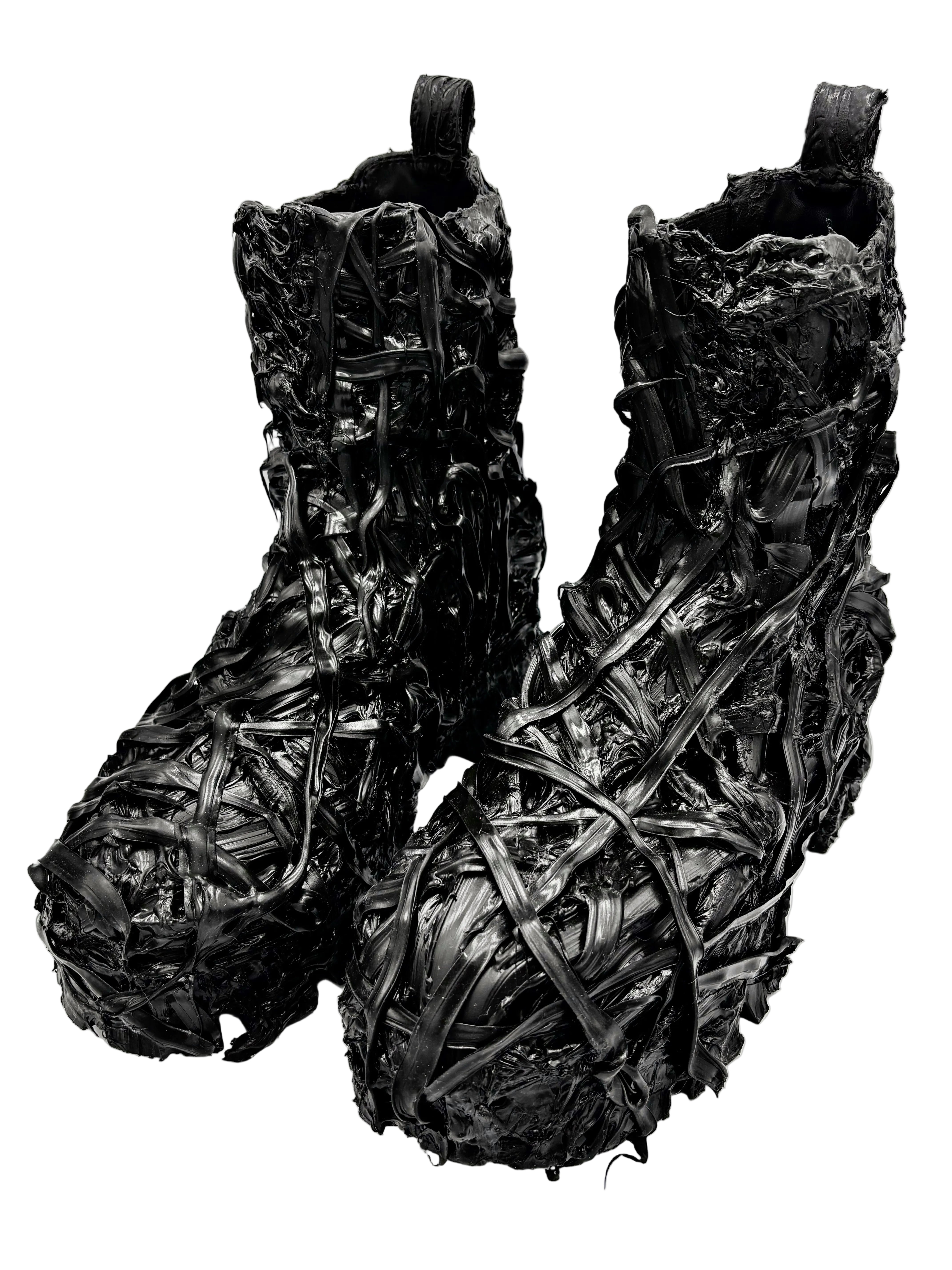 A pair of black textured boots with an intricate, woven, or shredded material surface, photographed against a plain white studio background.