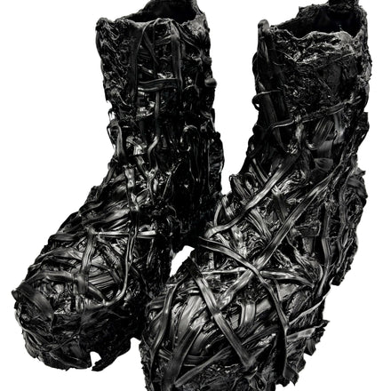 A pair of black textured boots with an intricate, woven, or shredded material surface, photographed against a plain white studio background.